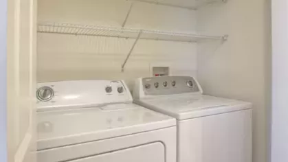 Full-sized washer and dryer set in a dedicated laundry nook with overhead shelving for convenient storage.