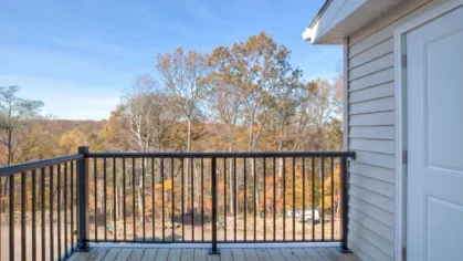 Private balcony with a black metal railing, overlooking a picturesque wooded landscape, perfect for enjoying the fresh air.