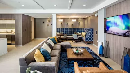 A stylish resident lounge at Vista At Town Green Luxury Apartments, offering plush seating, a mounted TV, and a cozy booth area with elegant blue accents.