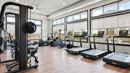 A fully equipped fitness center with treadmills, weight machines, and bright windows overlooking the pool area.