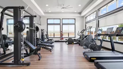 Another angle of the fitness center, featuring weight benches, ellipticals, and exercise balls under ample natural light.