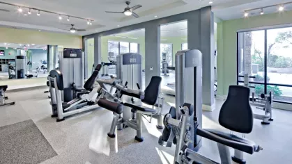A well-equipped strength training area at Vista At Town Green Luxury Apartments, featuring weight machines, large mirrors, and ample natural light.