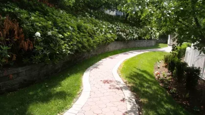 A serene community walkway at Vista At Town Green Luxury Apartments, winding through lush landscaping, vibrant flowers, and manicured greenery.