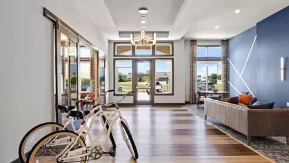 A modern communal lounge area with bicycles near the entrance, featuring a blue accent wall, large windows, and cozy seating arrangements.