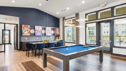 A stylish entertainment space featuring a pool table, dining table, and vibrant artwork on the navy accent wall, with ample natural light through floor-to-ceiling windows.