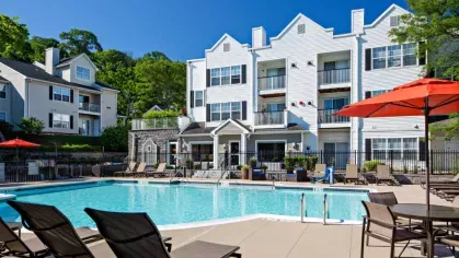 Large swimming pool with elegant white apartment buildings in the background, surrounded by sun loungers and vibrant orange umbrellas.