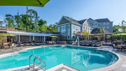 Resort-style swimming pool at Vista At Town Green Luxury Apartments, featuring crystal-clear water, shaded lounge chairs, and a clubhouse with modern architecture in the background.