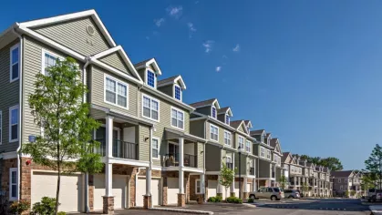 A tree-lined street with modern townhomes, private garage entries, and a serene suburban atmosphere at Vista At Town Green Luxury Apartments.