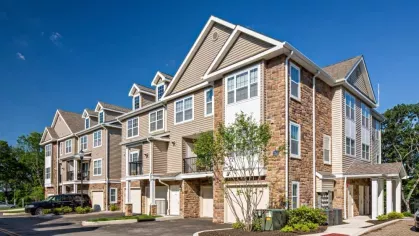 Modern townhome buildings at Vista At Town Green, featuring elegant stone accents, attached garages, and lush landscaping under a clear blue sky.