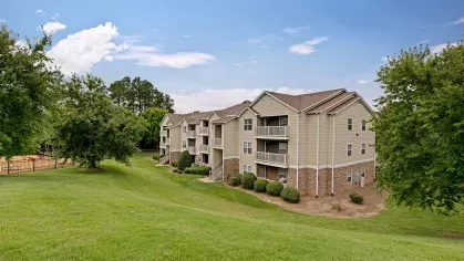 Beige apartment complex surrounded by lush greenery with a playground visible in the background."