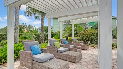 Relaxing outdoor seating under a white pergola with wicker chaise lounges and colorful pillows in a tropical garden setting.