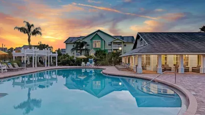 Stunning pool at sunset with warm, colorful skies reflecting off the water and charming light blue and green apartment buildings.
