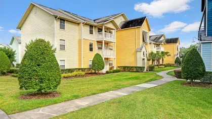 Yellow apartment buildings with white balconies, manicured lawns, and a paved walkway.