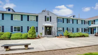 Blue and gray building at Alcove at Seahurst with vibrant landscaping and a clean, open walkway.