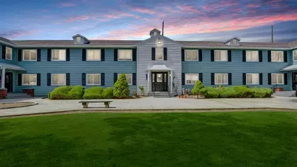 Blue multi-unit apartment building at Alcove at Seahurst with a well-maintained lawn and a beautiful sunset sky.