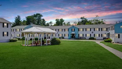 Central courtyard at Alcove at Seahurst featuring a white gazebo, picnic tables, and green open space against a colorful sunset.
