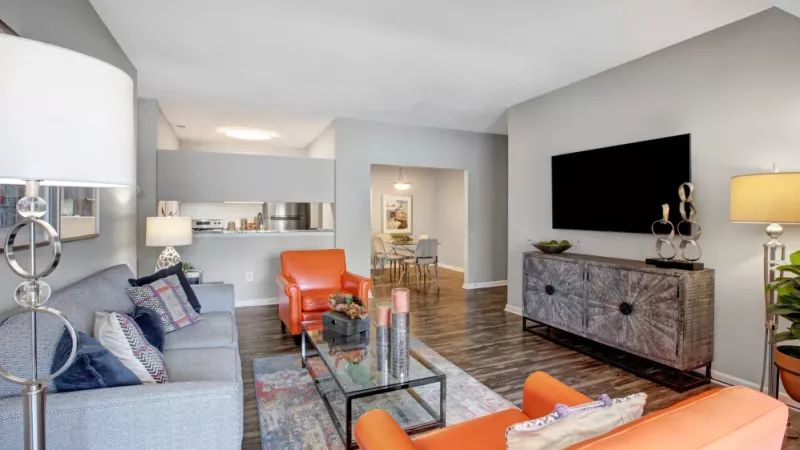 Living area with a gray sofa, orange chairs, a flat-screen TV, and eclectic decor in a spacious apartment.