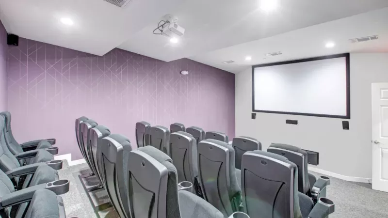 Community movie theater room with plush seating, a large screen, and purple geometric accent wall.