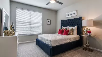 A cozy bedroom with a tufted navy headboard, red accent pillows, and a ceiling fan, creating a relaxing space.