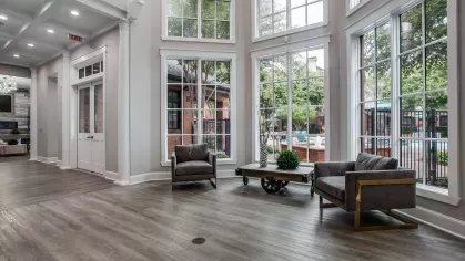 A spacious and elegant lounge with natural light, modern furnishings, and a view of the outdoor pool.