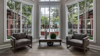 A spacious and elegant lounge with natural light, modern furnishings, and a view of the outdoor pool.