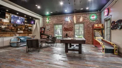 A stylish game room featuring a pool table, vintage arcade games, and neon signage on exposed brick walls.