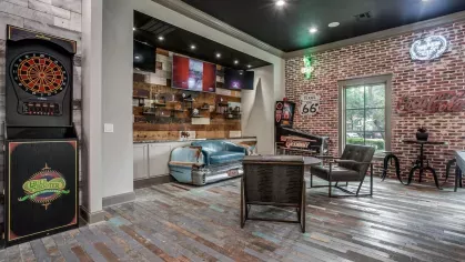 A lounge with a pool table, vintage signs, arcade games, and a reclaimed wood floor.
