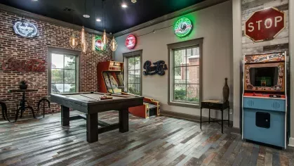 A lounge with a pool table, vintage signs, arcade games, and a reclaimed wood floor.