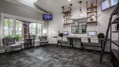 A business center with comfortable seating, computer workstations, and rustic shelves against a white brick wall.