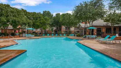 A large swimming pool surrounded by lush trees, comfortable lounge chairs, and shaded seating areas.