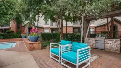 A cozy poolside lounge with turquoise cushioned chairs, a built-in grill, and brick pavers.