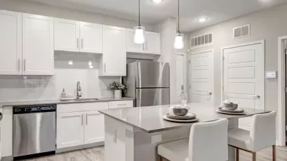 A modern kitchen with white cabinetry, stainless steel appliances, and a large island with two white barstools.