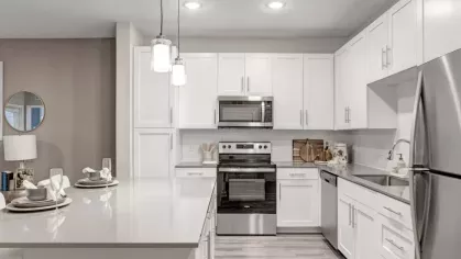 A sleek kitchen featuring a white color scheme, a stainless steel refrigerator, and a spacious island with pendant lighting.