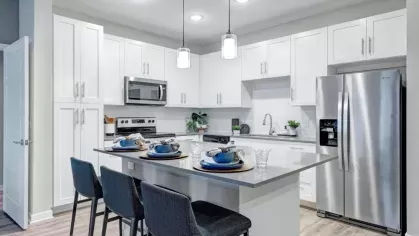 A stylish kitchen with white cabinetry, a stainless steel refrigerator, and a gray island set for dining with blue dishware.