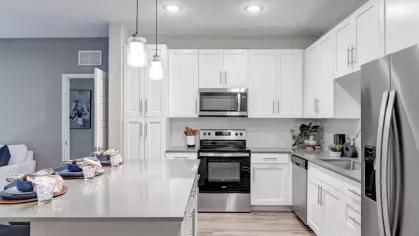 A well-lit kitchen showcasing white cabinets, stainless steel appliances, and a breakfast bar with navy barstools.