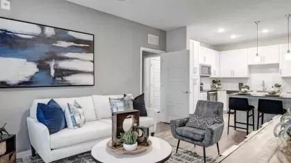 A sophisticated living room with a wall-mounted TV, plush seating, and an adjoining open-concept kitchen.