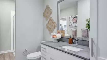 A modern bathroom with a sleek gray countertop, white cabinetry, and decorative wall art above the toilet.