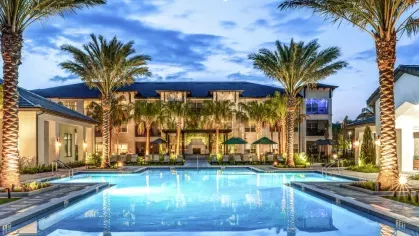 A beautifully illuminated pool area at dusk, reflecting palm trees and the surrounding modern apartments.