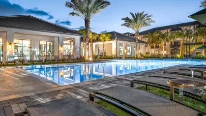 A luxurious pool deck with lounge chairs, overlooking a pristine blue pool with modern apartment buildings in the background.