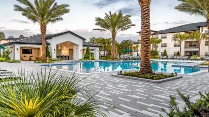 A tranquil poolside setting with lounge seating and a clubhouse, surrounded by vibrant greenery and palm trees.