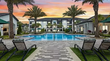 A vibrant sunset casts warm hues over a resort-style pool with lounge chairs and lush landscaping.