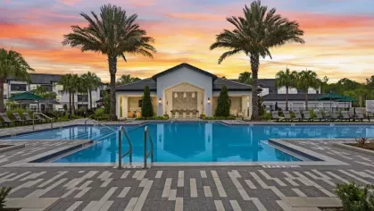A tranquil pool area at dusk, with soft lighting reflecting on the water and tropical landscaping.