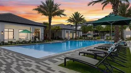 A resort-style poolside retreat with lounge chairs and large umbrellas, set against a colorful sunset.