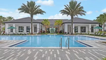 A symmetrical view of a pool with a contemporary clubhouse and palm trees under a blue sky.