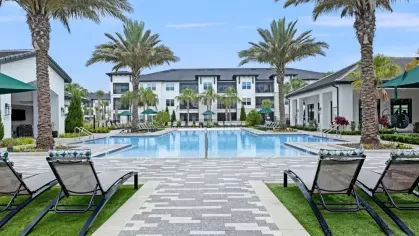 A spacious pool area with a well-manicured deck, palm trees, and modern poolside furniture.