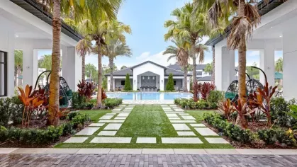 A beautifully landscaped pathway lined with palm trees leading to a serene swimming pool.
