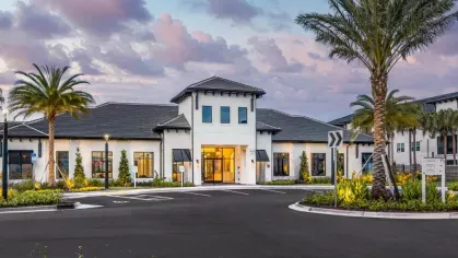 The front entrance of a stylish clubhouse with warm lighting and a landscaped roundabout.