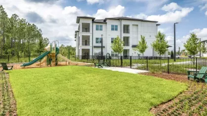 A spacious grassy play area with a playground, set against modern apartment buildings.