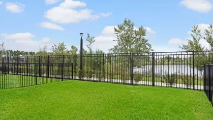 A fenced-in grassy area overlooks a serene lake with trees and walking paths in the background.