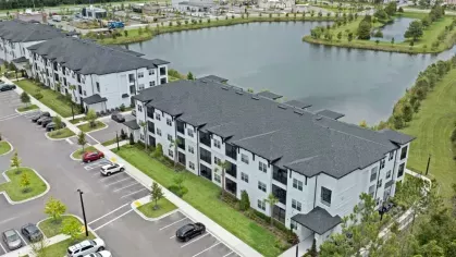Aerial shot of the apartment buildings near a scenic lake, with parking lots and green spaces surrounding the complex.